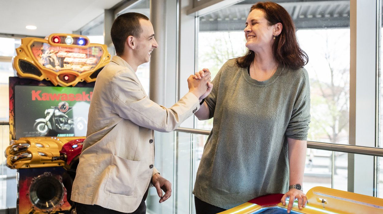 Zwei Personen geben sich die Hand, im Hintergrund steht ein Spielautomat