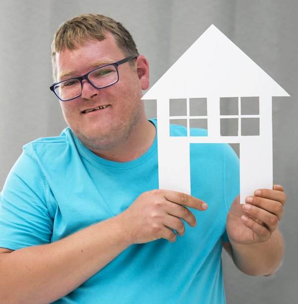 ein Mann mit Behinderung hält freudig ein Papierhaus in der Hand