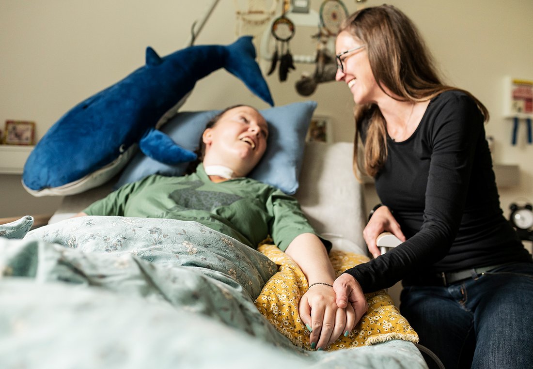 Eine Begleiterin sitzt am Bett einer Frau mit Behinderung