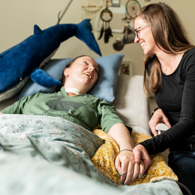 Eine Begleiterin sitzt am Bett einer Frau mit Behinderung
