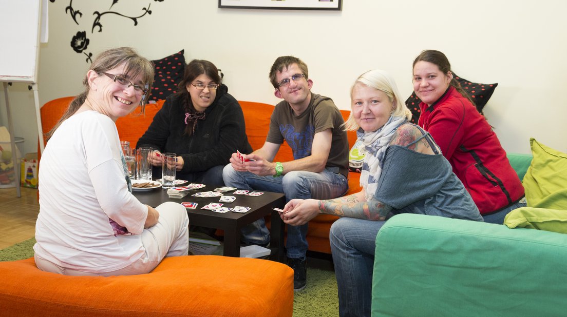 Menschen mit Behinderung und Betreuerinnen spielen sitzend auf einer Couch Uno