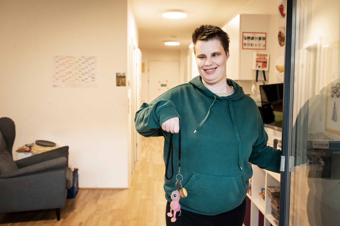 Eine Frau mit Behinderung steht in der Eingangstür und hält einen schlüssel hoch