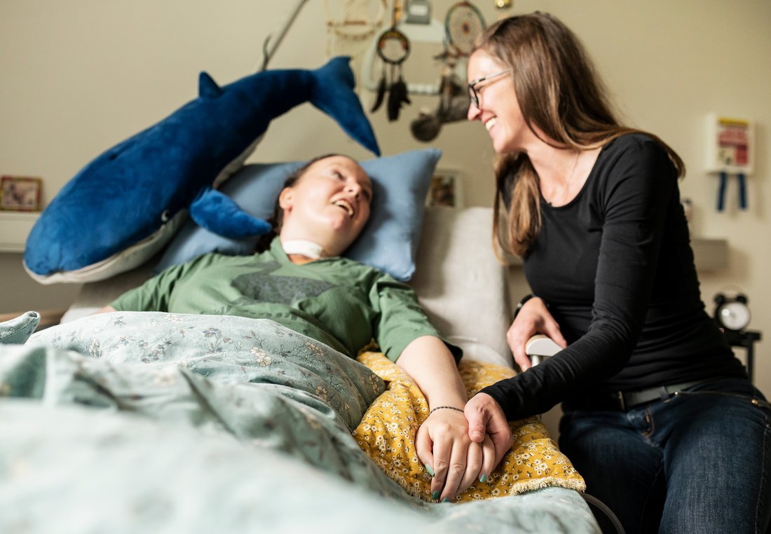 Eine Begleiterin sitzt am Bett einer Frau mit Behinderung
