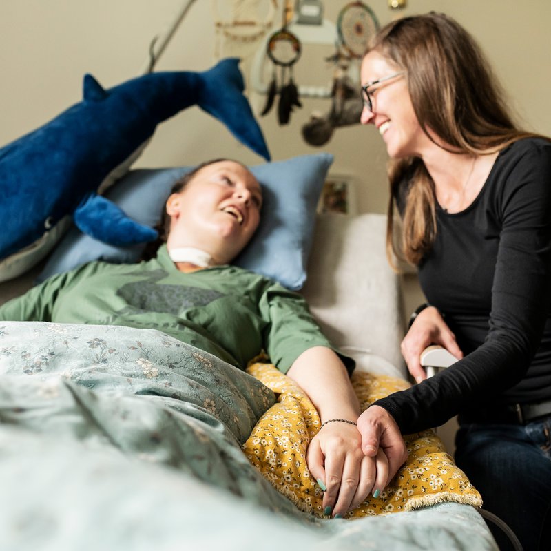 Eine Begleiterin sitzt am Bett einer Frau mit Behinderung