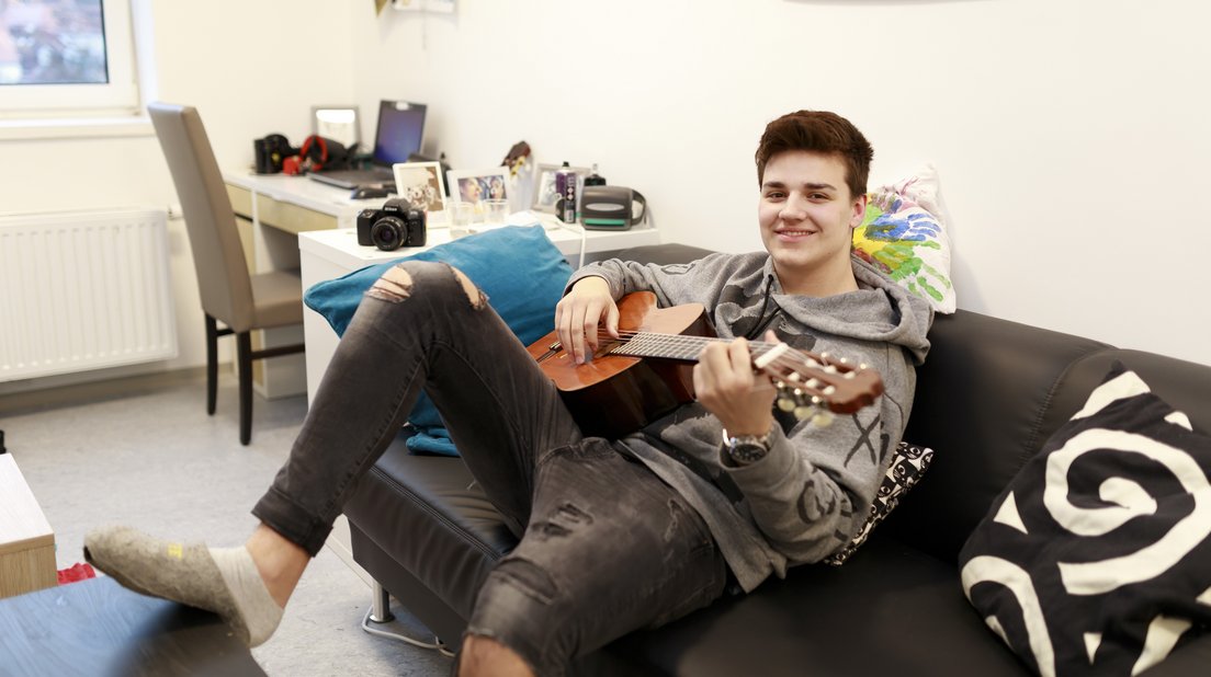 ein Jugendlicher spielt Gitarre auf einer Couch