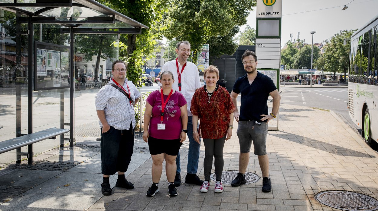 Fünf Mobilitätstrainer*innen stehen an der Bushaltestelle