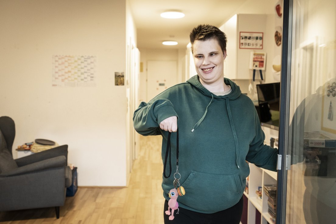 Eine Frau mit Behinderung steht in der Eingangstür und hält einen schlüssel hoch