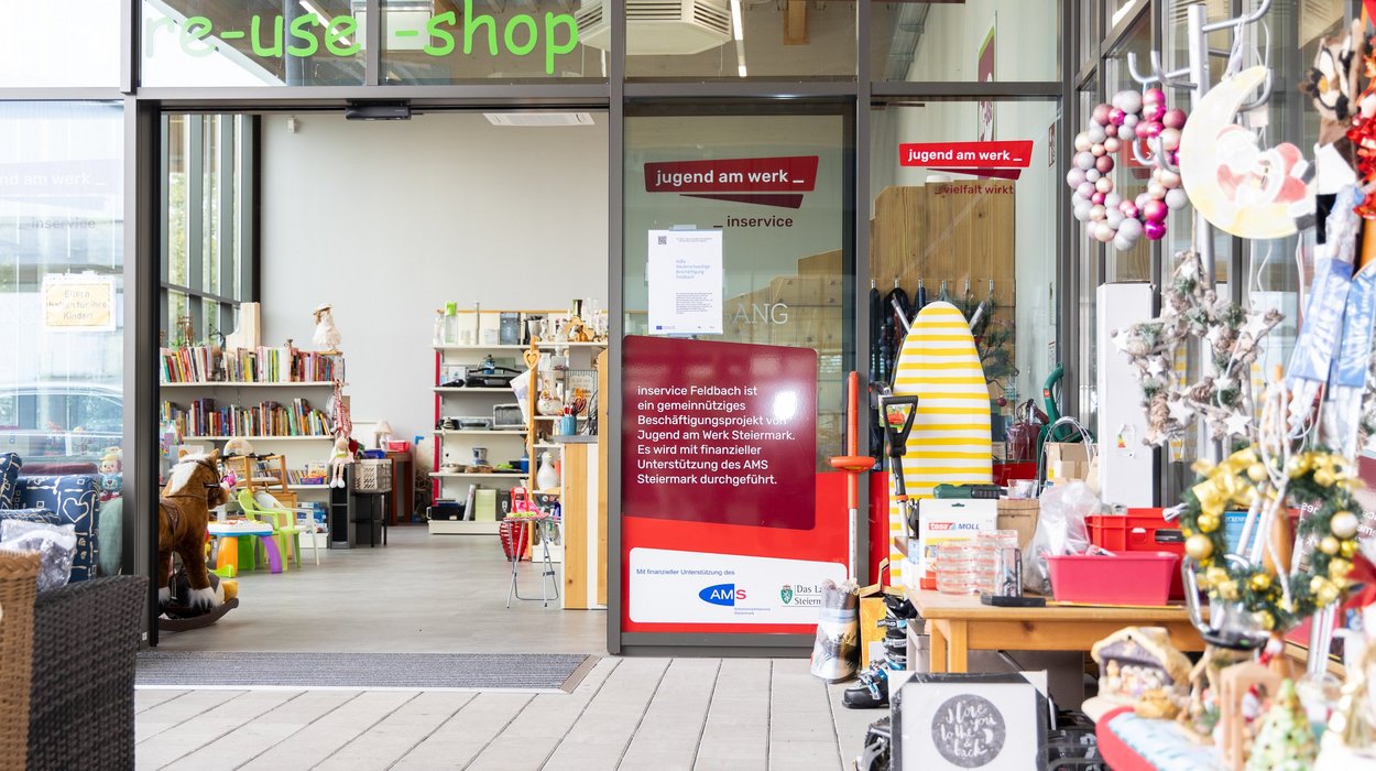 Vorderansicht eines Shops mit großer Glasfront und dem grünen Schriftzug "re use shop" darauf