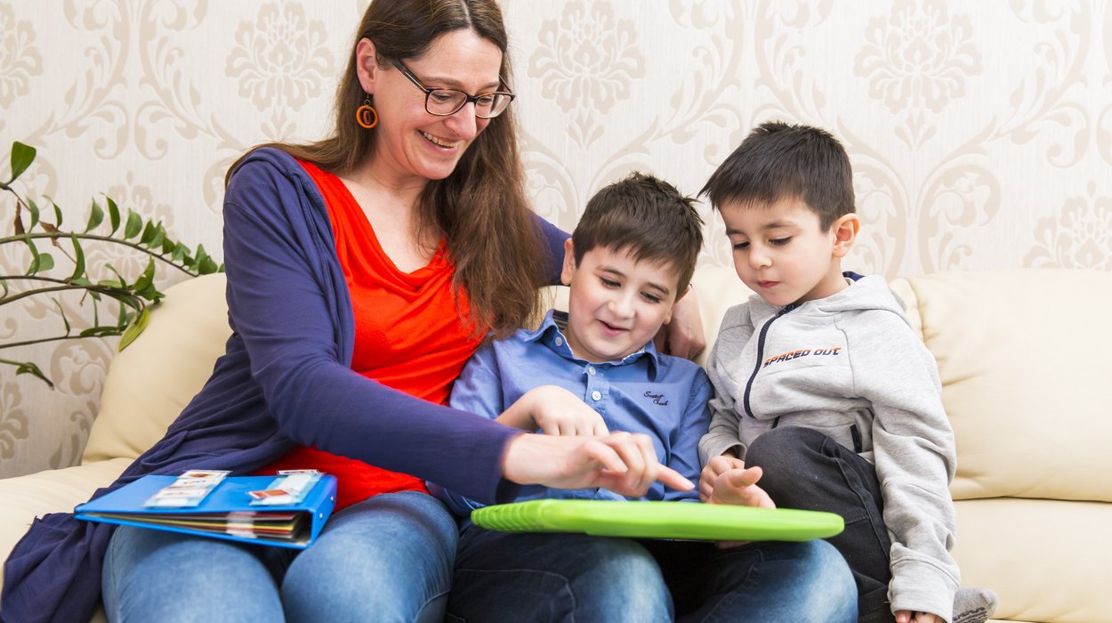 eine Betreuern lernt mit zwei Kindern mit einem Kommunikationslerngerät