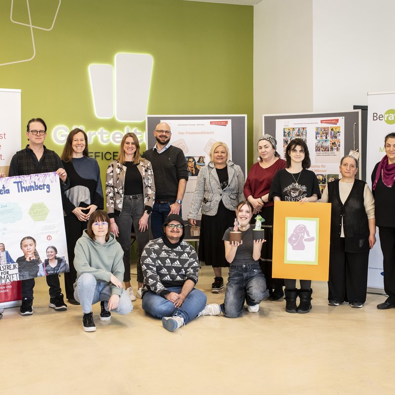 Eine Gruppe Menschen mit bunten Ausstellungsplakaten im Foyer eines Gebäudes