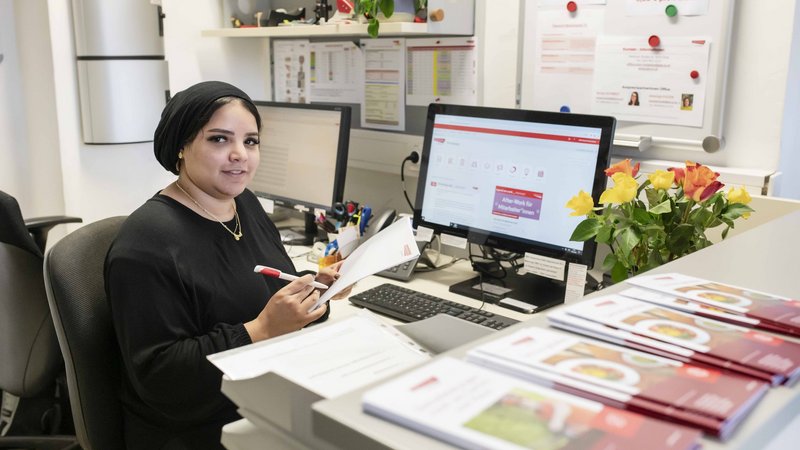 Frau an einem Empfang, sitzt vor einem Computer und schreibt gerade etwas auf